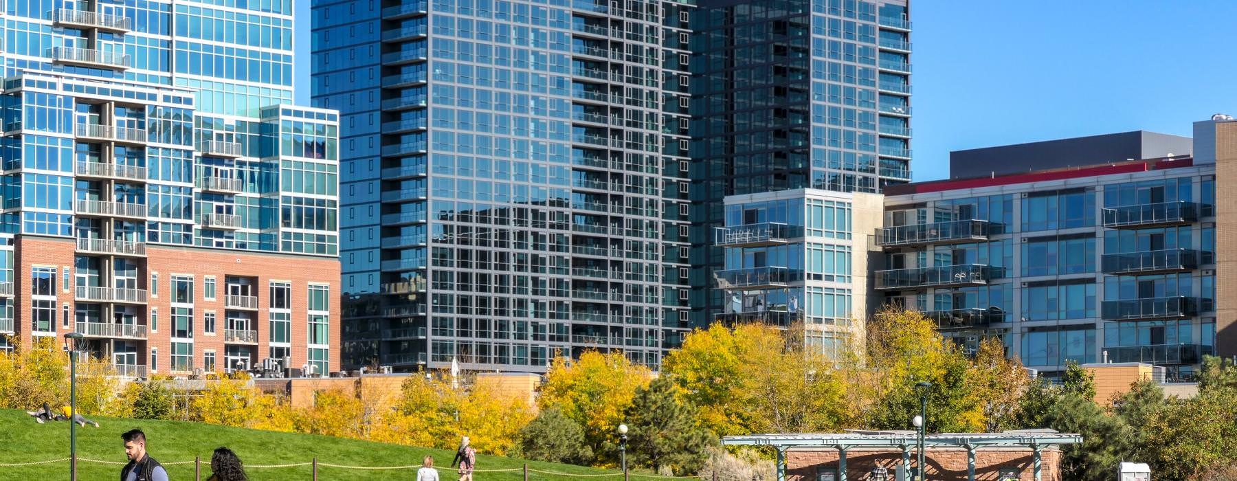 a group of people walking in a park in front of a group of buildings